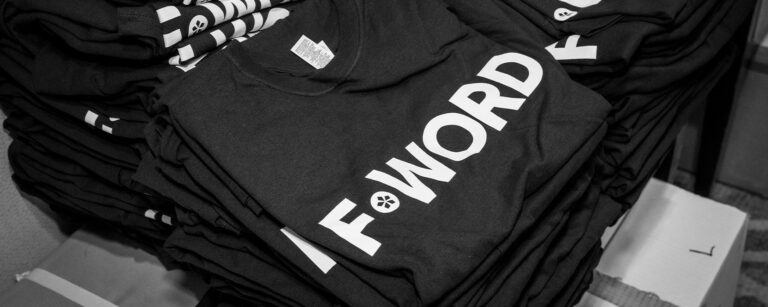 Piles of F-Word t-shirts folded on a table.