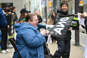 Member chants into a megaphone while sitting down.
