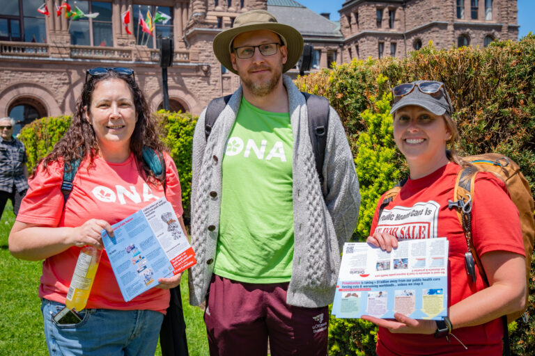 Three members standing in a row hold OHC pamphlets.
