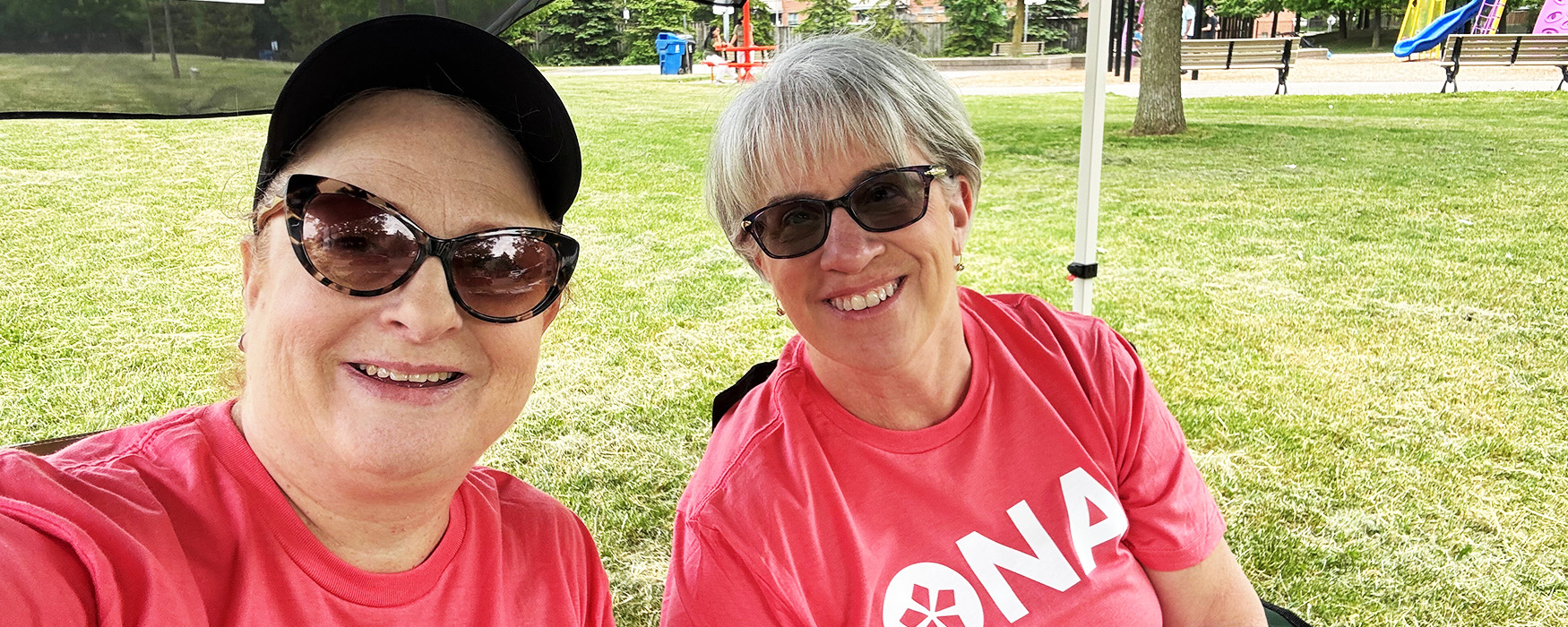 Two woman in ONA t-shirts smile at the camera.