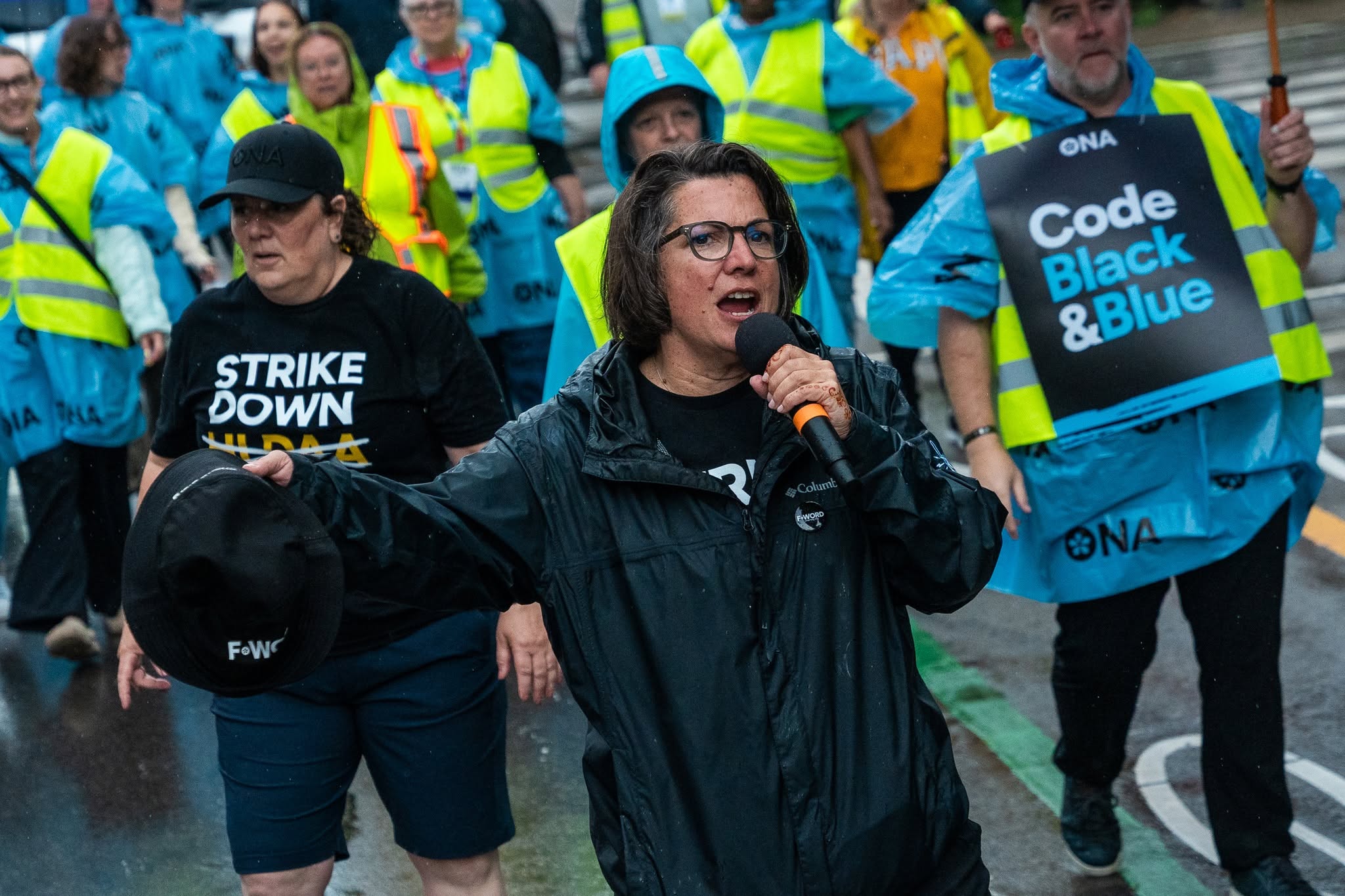 ONA Provincial President Erin Ariss speaks into a microphone with members rallying behind her.