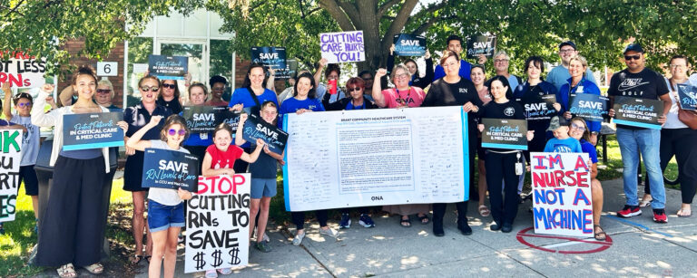 A large group surrounding a banner petition holds signs and fist pumps.