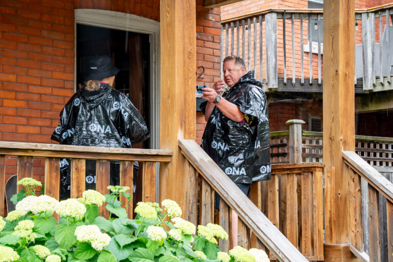 A man and a woman wearing rain ponchos stand at the open door of a house.