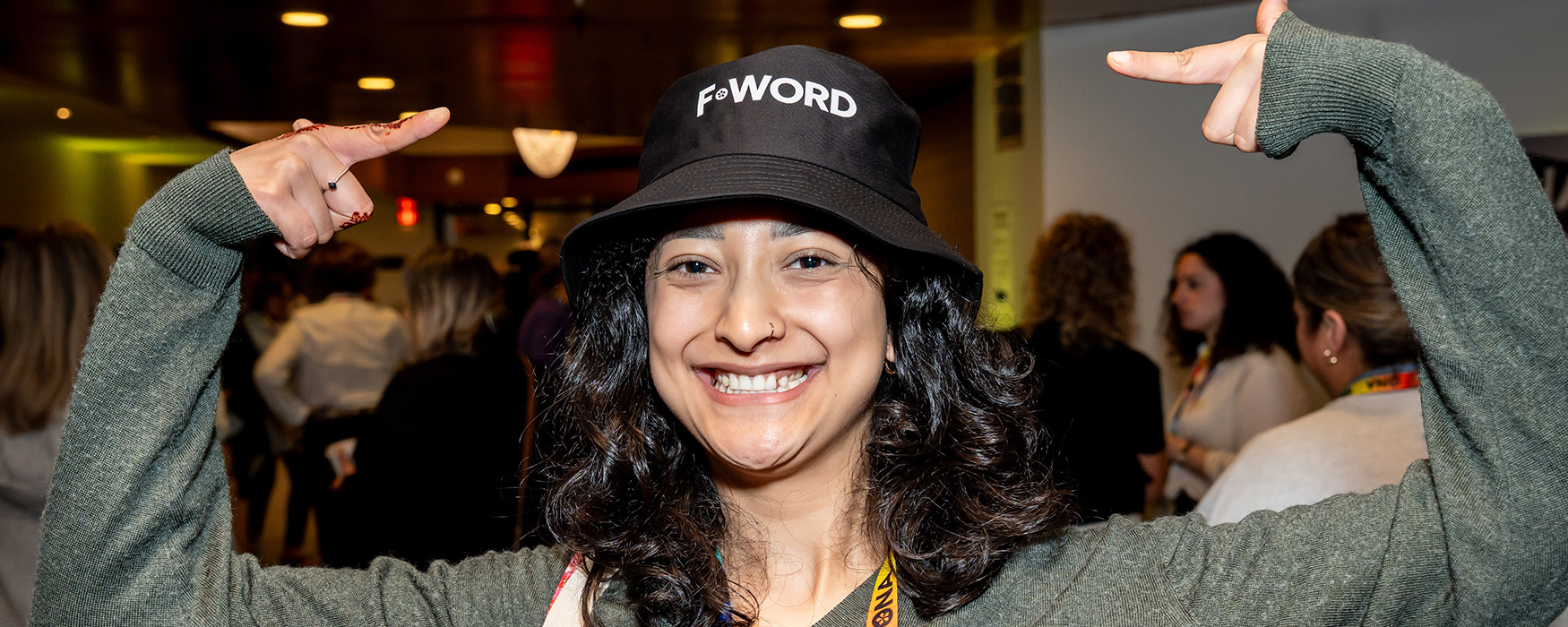 A woman points to her bucket hat, which reads F-Word.