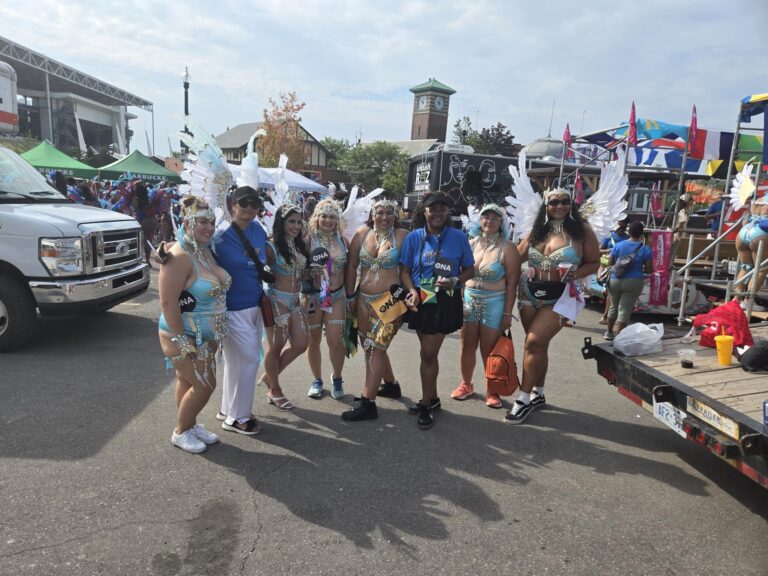 ONA member Leslie Davis is surrounded by other members, most dressed in colourful Carnival costumes.