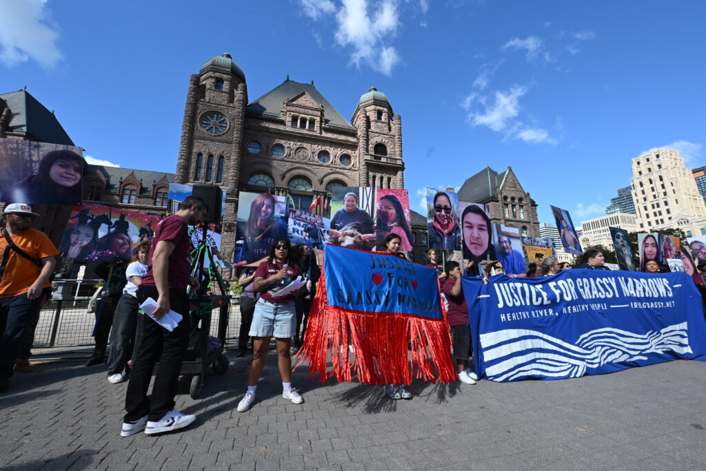 Woman addresses the crowd at Queen’s Park surrounded by photos and banners.