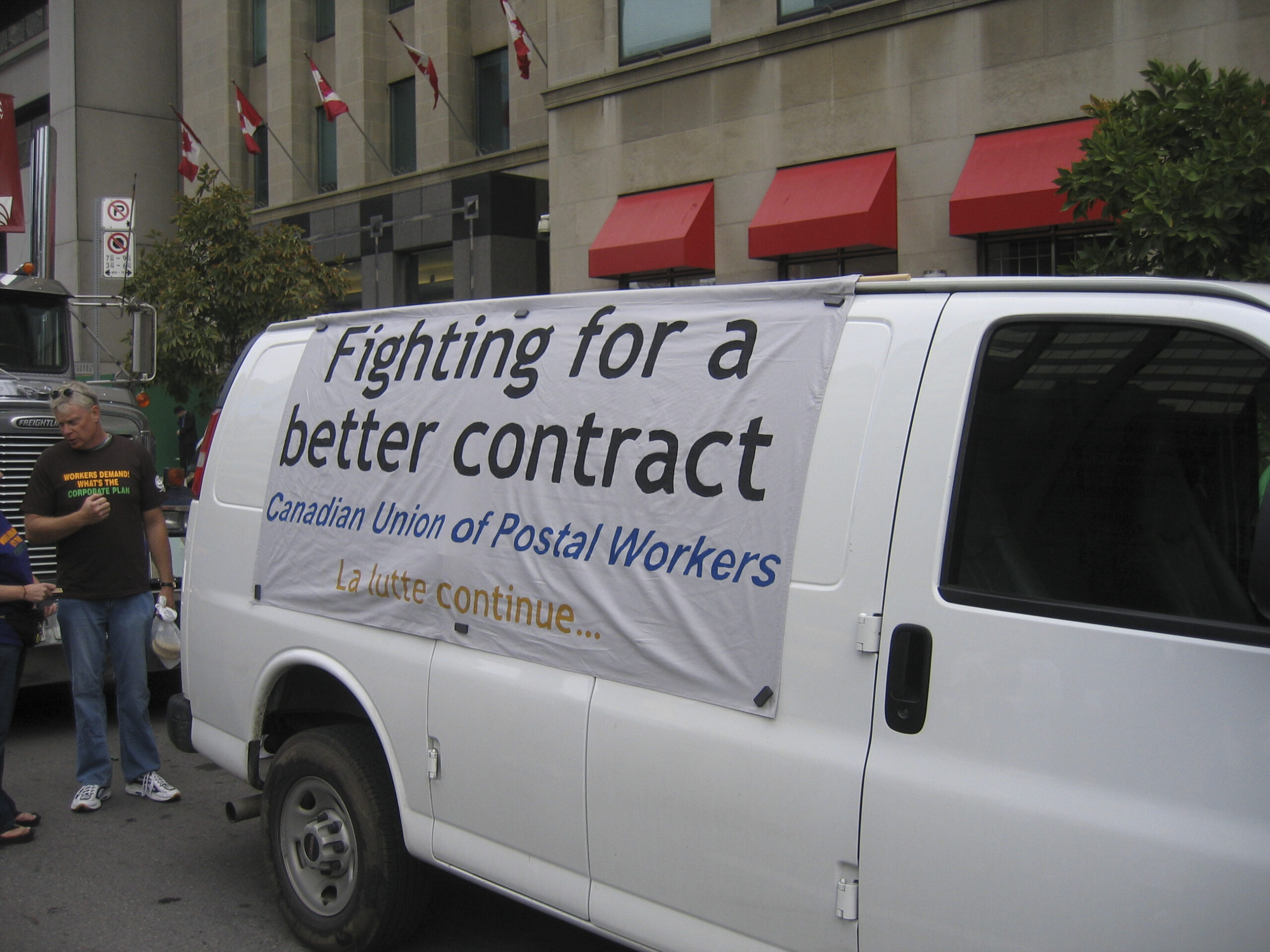 A parked white van displays a sign reading, “Fighting for a Better Contract, Canadian Union of Postal Workers.”